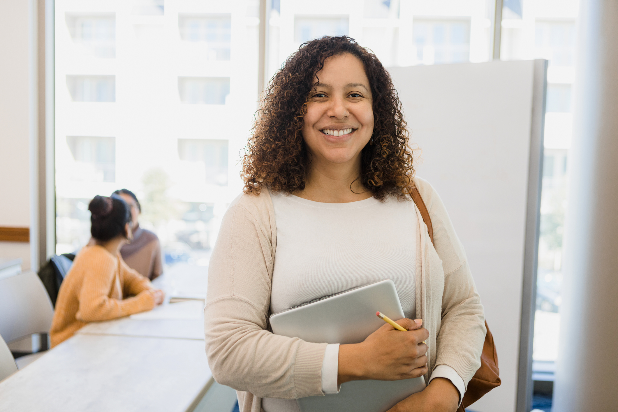 Non-traditional female college student holding laptop smiles for camera.